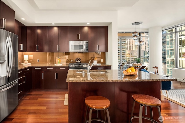 kitchen featuring appliances with stainless steel finishes, hardwood / wood-style floors, pendant lighting, sink, and light stone countertops