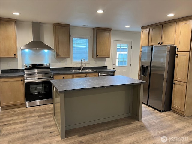 kitchen with wall chimney range hood, sink, appliances with stainless steel finishes, a kitchen island, and light wood-type flooring