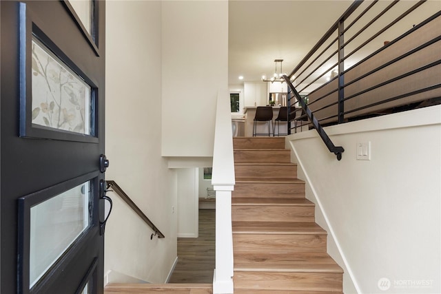 stairs with wood-type flooring and a notable chandelier