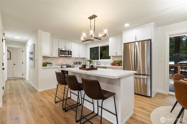 kitchen with hanging light fixtures, stainless steel appliances, a center island, tasteful backsplash, and white cabinets