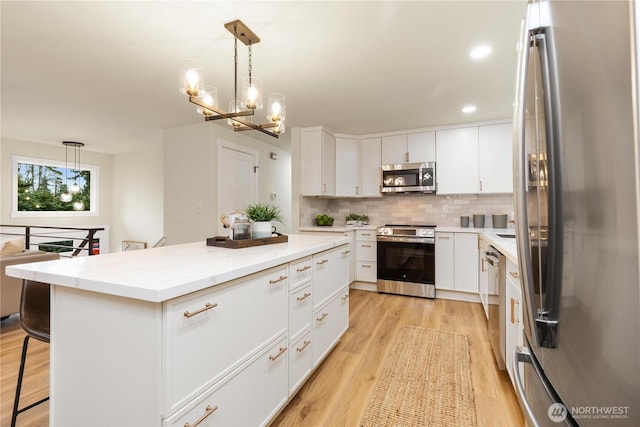 kitchen with stainless steel appliances, hanging light fixtures, a breakfast bar area, and white cabinets