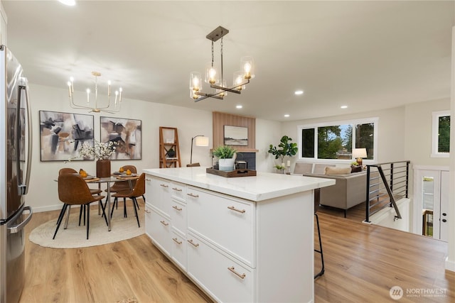 kitchen featuring pendant lighting, stainless steel refrigerator, white cabinets, a chandelier, and a center island