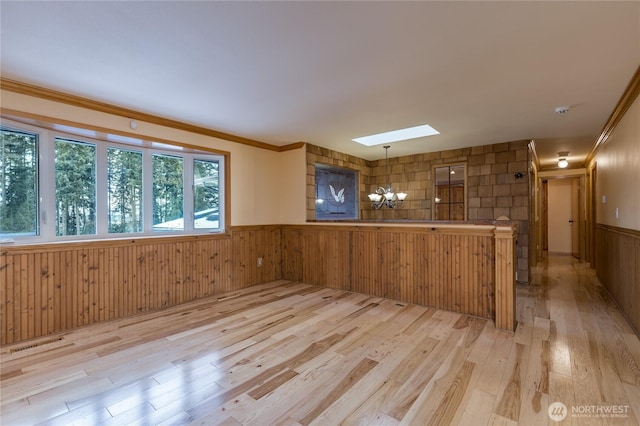 interior space featuring hanging light fixtures, light wood-type flooring, wainscoting, and a skylight