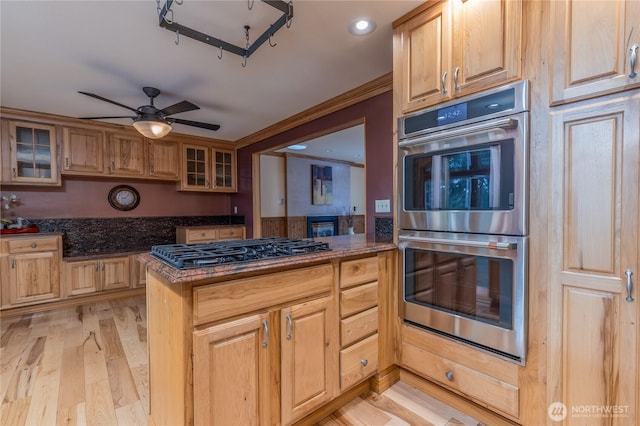 kitchen featuring ceiling fan, stainless steel appliances, light wood finished floors, glass insert cabinets, and crown molding