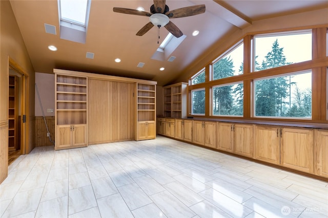 unfurnished living room featuring lofted ceiling with skylight, ceiling fan, wainscoting, and recessed lighting