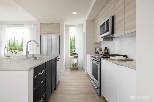 kitchen with sink, appliances with stainless steel finishes, light stone counters, light hardwood / wood-style floors, and light brown cabinetry
