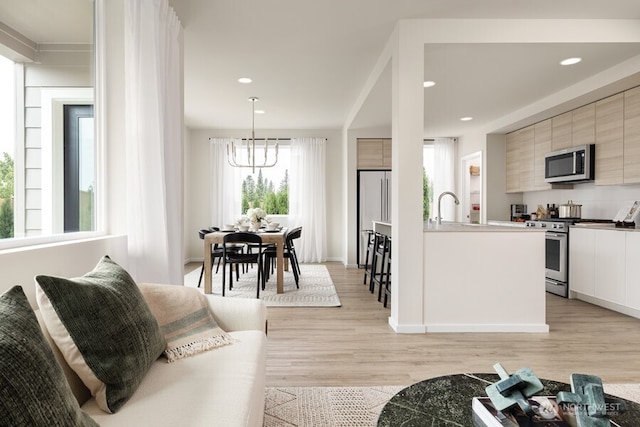 kitchen featuring sink, an inviting chandelier, hanging light fixtures, stainless steel appliances, and light hardwood / wood-style floors