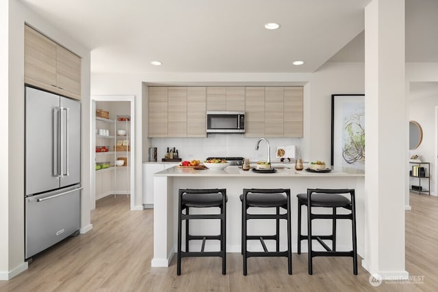 kitchen with appliances with stainless steel finishes, a breakfast bar, kitchen peninsula, and light wood-type flooring