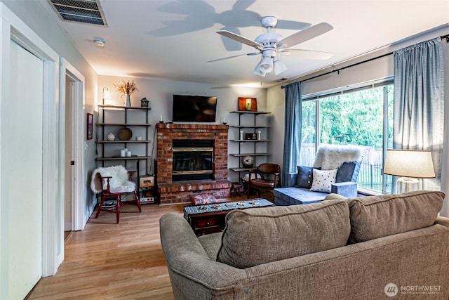 living room featuring ceiling fan, light wood-type flooring, visible vents, and a brick fireplace