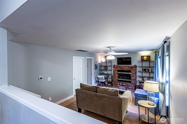 living room featuring baseboards, visible vents, ceiling fan, wood finished floors, and a fireplace