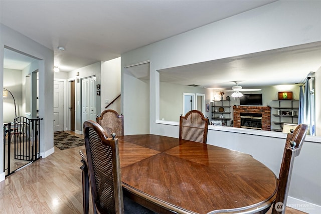 dining area with a brick fireplace, ceiling fan, baseboards, and light wood-style floors