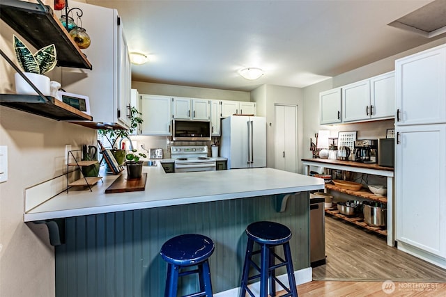 kitchen featuring a breakfast bar area, a peninsula, white appliances, white cabinets, and light countertops