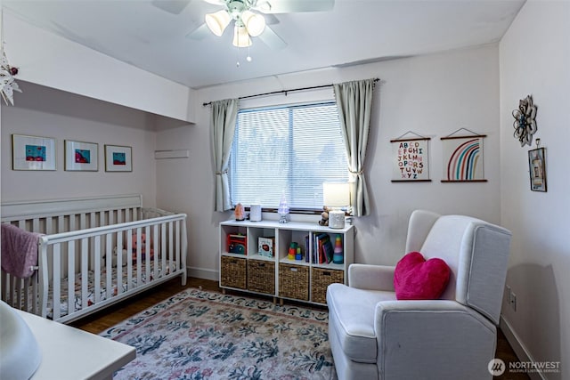 bedroom featuring a crib, ceiling fan, baseboards, and wood finished floors