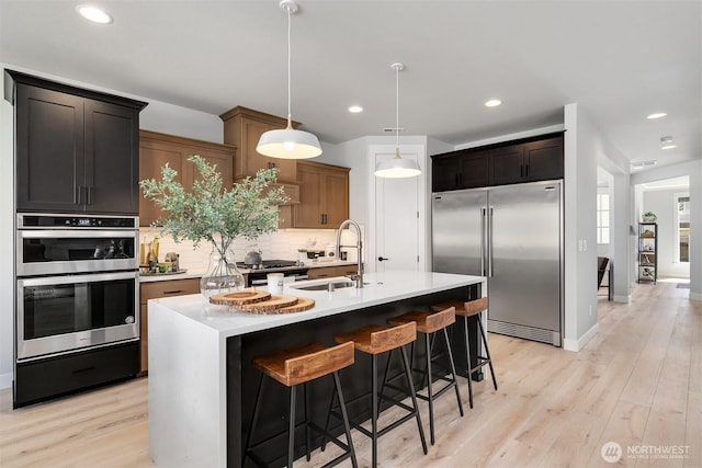 kitchen featuring appliances with stainless steel finishes, decorative light fixtures, a kitchen island with sink, light countertops, and a sink