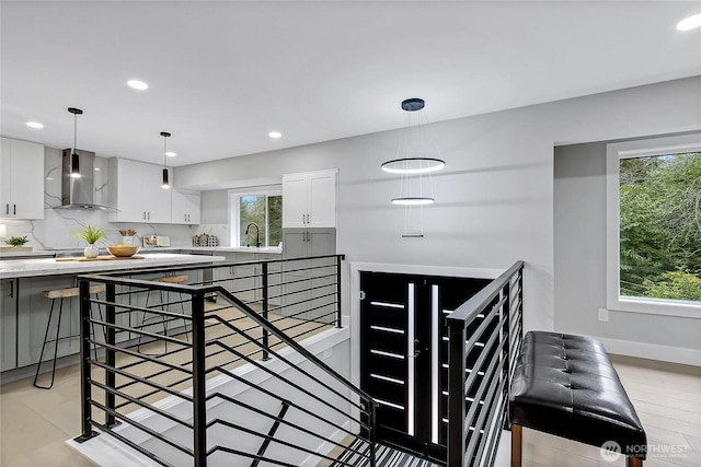 kitchen featuring hanging light fixtures, a healthy amount of sunlight, white cabinets, and wall chimney exhaust hood