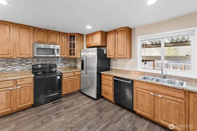 kitchen featuring dark wood-type flooring, sink, light stone countertops, decorative backsplash, and black appliances