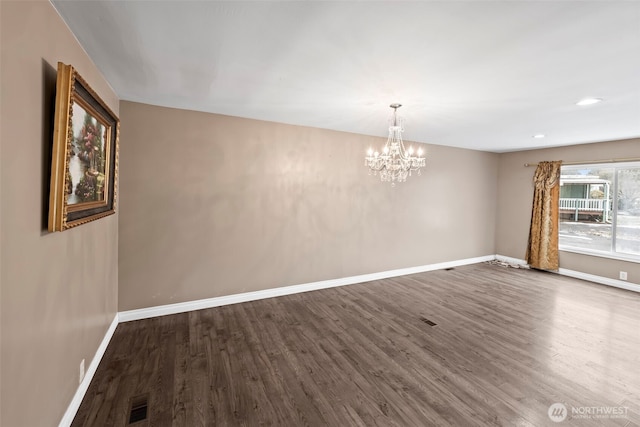 spare room with dark wood-type flooring and a chandelier