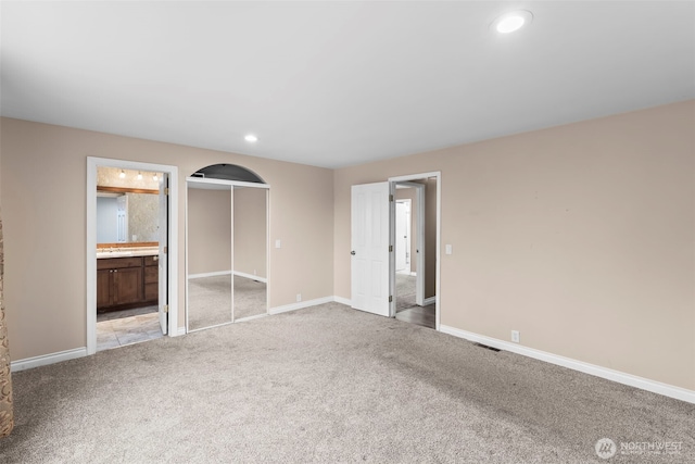 unfurnished bedroom with connected bathroom, light colored carpet, and a closet