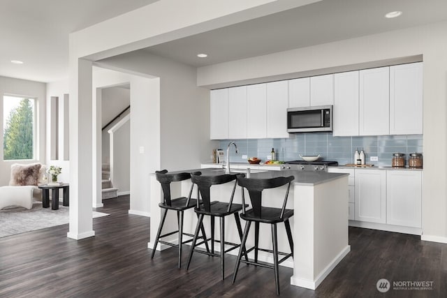 kitchen featuring white cabinetry, an island with sink, backsplash, a kitchen breakfast bar, and dark hardwood / wood-style flooring
