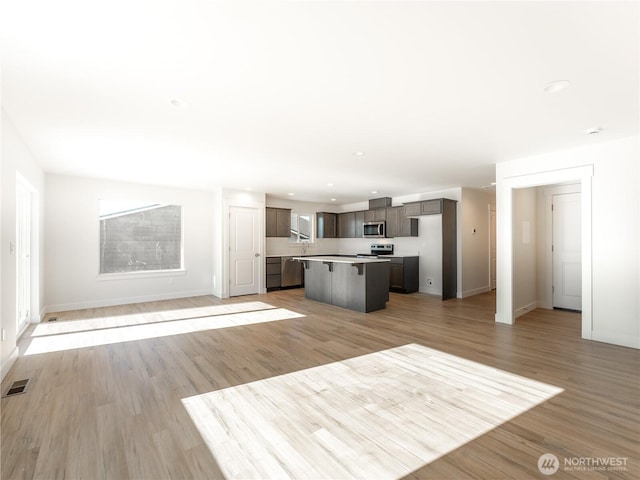 kitchen featuring light hardwood / wood-style flooring, a breakfast bar, stainless steel appliances, a center island, and dark brown cabinetry