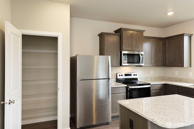 kitchen with stainless steel appliances, light stone countertops, and dark brown cabinets