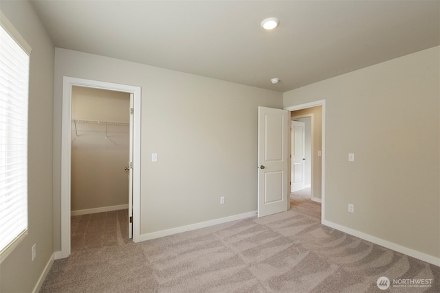 unfurnished bedroom with a walk in closet, light colored carpet, and a closet