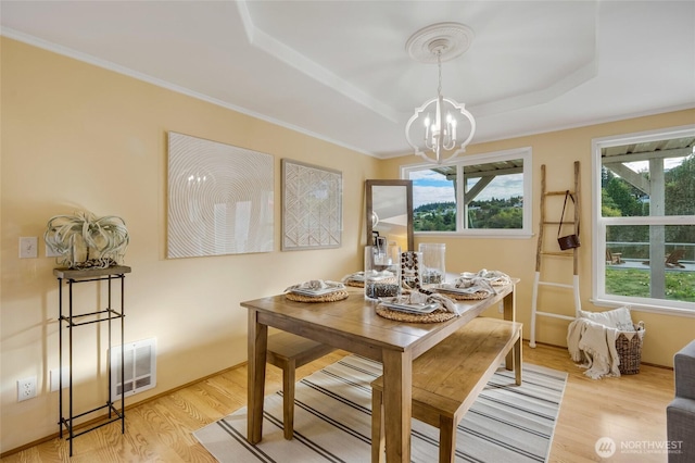 dining space with visible vents, a raised ceiling, an inviting chandelier, a healthy amount of sunlight, and light wood finished floors