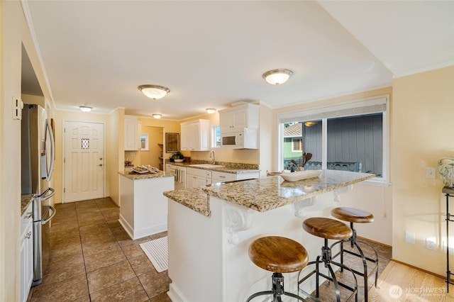kitchen featuring a center island, stainless steel refrigerator with ice dispenser, a breakfast bar, crown molding, and white microwave