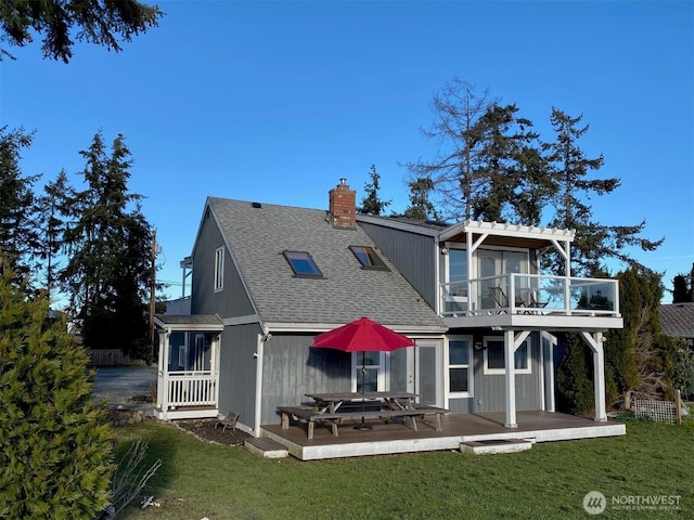 rear view of house featuring a chimney, a balcony, a yard, and roof with shingles