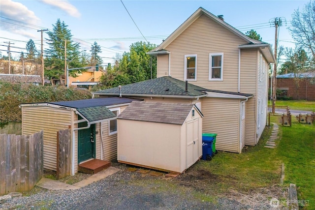 back of house with a storage shed, fence, a lawn, and an outdoor structure