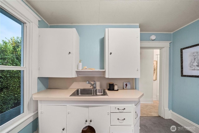 kitchen featuring ornamental molding, a sink, white cabinets, light countertops, and baseboards