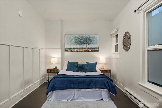 bedroom featuring a baseboard radiator, wood finished floors, wainscoting, and a decorative wall