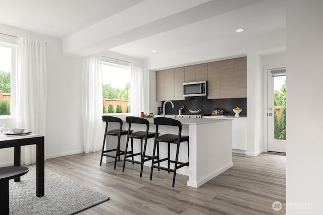 kitchen with light hardwood / wood-style flooring, a breakfast bar, a center island with sink, and decorative backsplash