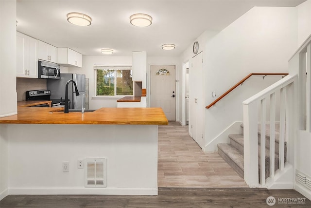 kitchen with white cabinetry, appliances with stainless steel finishes, light hardwood / wood-style flooring, and kitchen peninsula