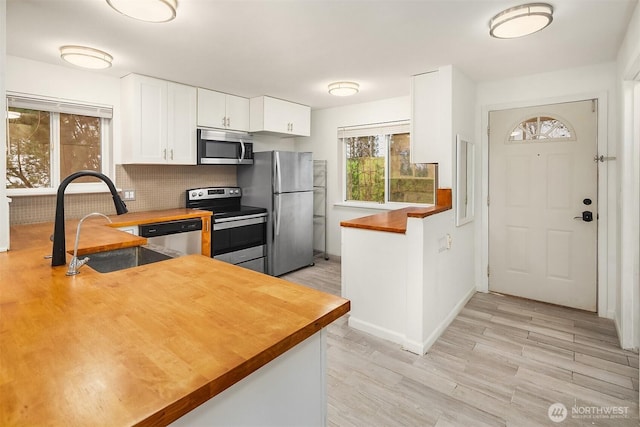 kitchen featuring appliances with stainless steel finishes, tasteful backsplash, sink, white cabinets, and wooden counters