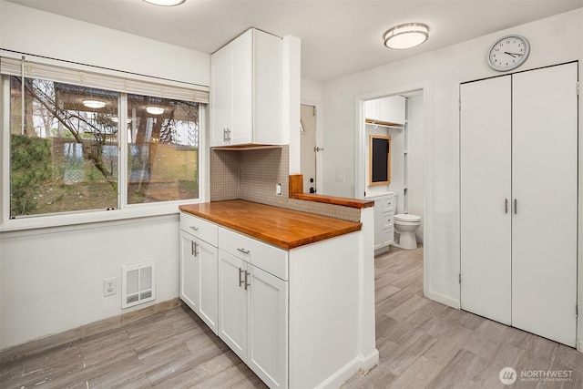 kitchen with white cabinetry, butcher block counters, backsplash, and light hardwood / wood-style flooring