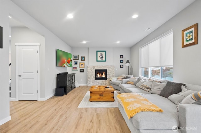 living area featuring light wood-type flooring, a stone fireplace, baseboards, and recessed lighting