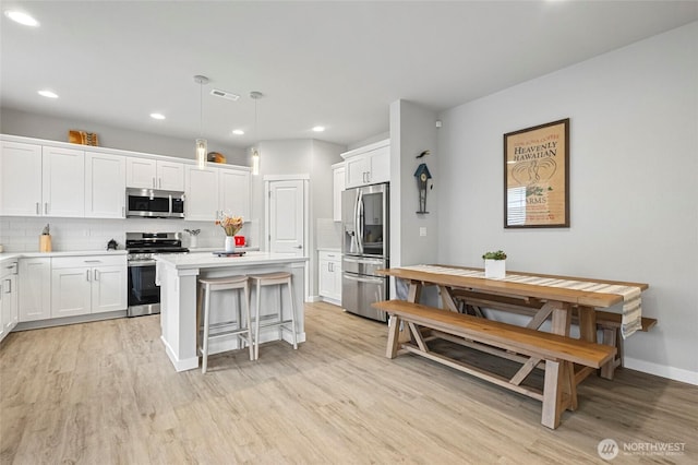 kitchen with light wood finished floors, visible vents, backsplash, appliances with stainless steel finishes, and a kitchen island