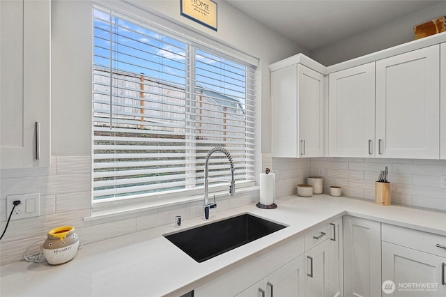 kitchen with tasteful backsplash, white cabinets, light countertops, and a sink