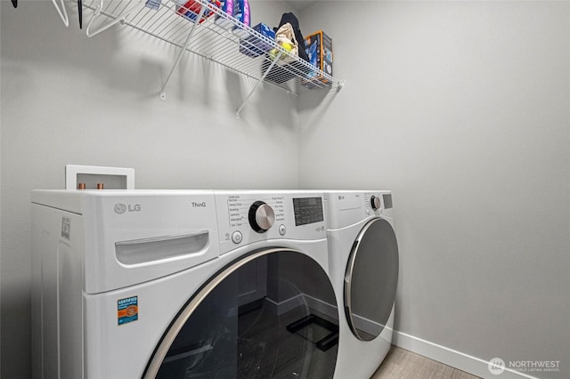 laundry area with laundry area, wood finished floors, washing machine and clothes dryer, and baseboards