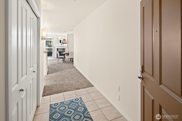 hallway featuring baseboards, light carpet, and light tile patterned flooring