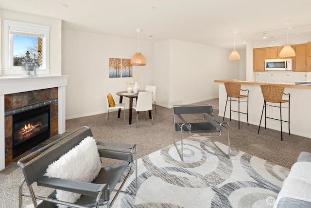 carpeted living area with a tile fireplace, rail lighting, and baseboards