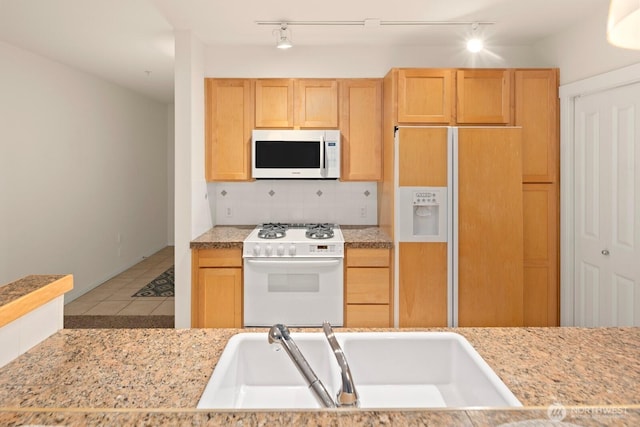 kitchen with tasteful backsplash, light brown cabinetry, tile patterned floors, white appliances, and a sink