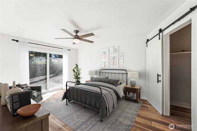 bedroom with ceiling fan, a barn door, wood finished floors, baseboards, and access to exterior