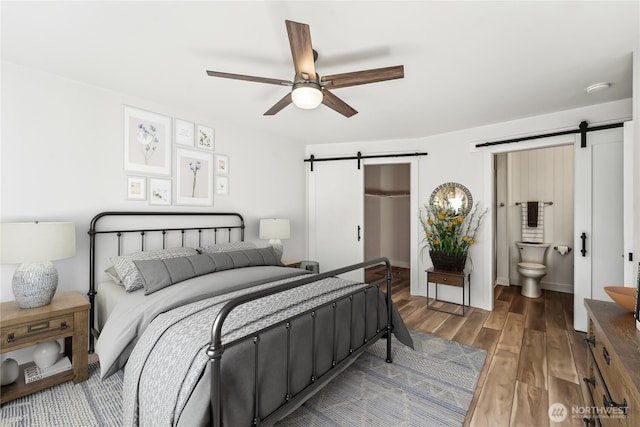 bedroom with a barn door, wood finished floors, a ceiling fan, a spacious closet, and a closet