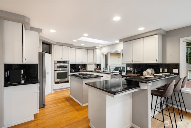 kitchen with white cabinetry, a kitchen breakfast bar, kitchen peninsula, stainless steel appliances, and light wood-type flooring