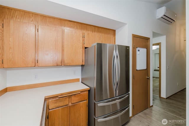 kitchen with a wall mounted air conditioner, stainless steel fridge, and light wood-type flooring