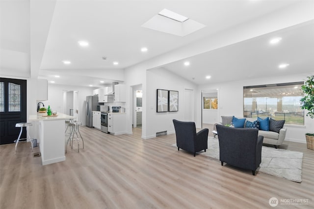 living room featuring sink, a wealth of natural light, light hardwood / wood-style floors, and vaulted ceiling with skylight