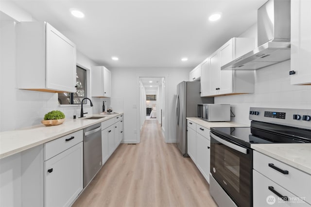 kitchen featuring light stone counters, wall chimney range hood, white cabinets, and appliances with stainless steel finishes