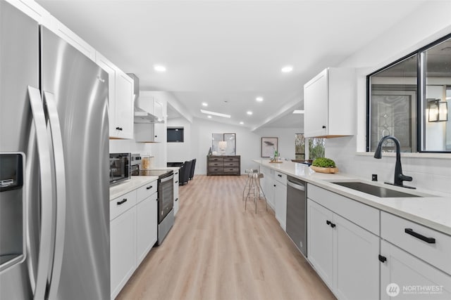 kitchen with sink, white cabinetry, stainless steel appliances, vaulted ceiling, and light wood-type flooring